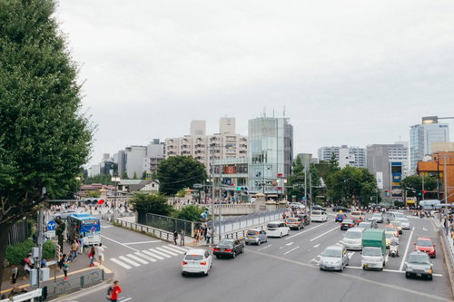原宿駅前の交差点で往来する人と車、高層ビル群の都会景観