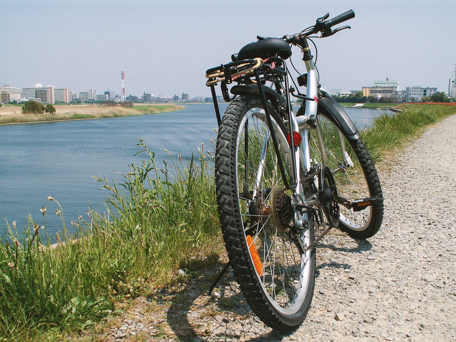 河川敷の砂利道にマウンテンバイクが停められ対岸に都市の建物群が見える