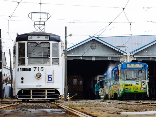 車庫に停車する白い路面電車と青い車両