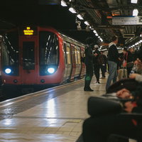 ロンドンの地下鉄駅に停車する赤色の電車と乗客の写真