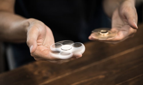 両手にハンドスピナーを握って回すシーン、木製テーブルでの同時回転