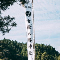 森に囲まれた古殿八幡神社の白いのぼり旗と社殿の写真