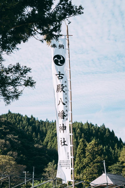 森に囲まれた古殿八幡神社の白いのぼり旗と社殿