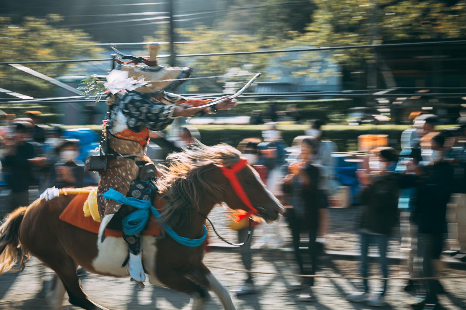 古殿八幡神社の境内で矢を構える流鏑馬の騎手が馬で駆け抜ける