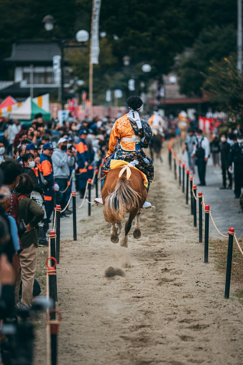 古殿八幡神社の例大祭で、錦織の衣装を着た騎手が馬に乗り、観客に見守られながら流鏑馬を行っている