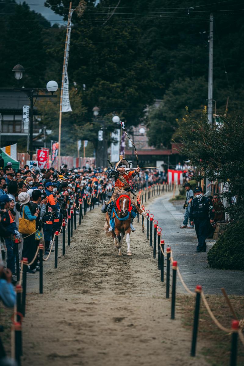 古殿八幡神社の流鏑馬で赤い装束の騎手が馬上で弓を構えている