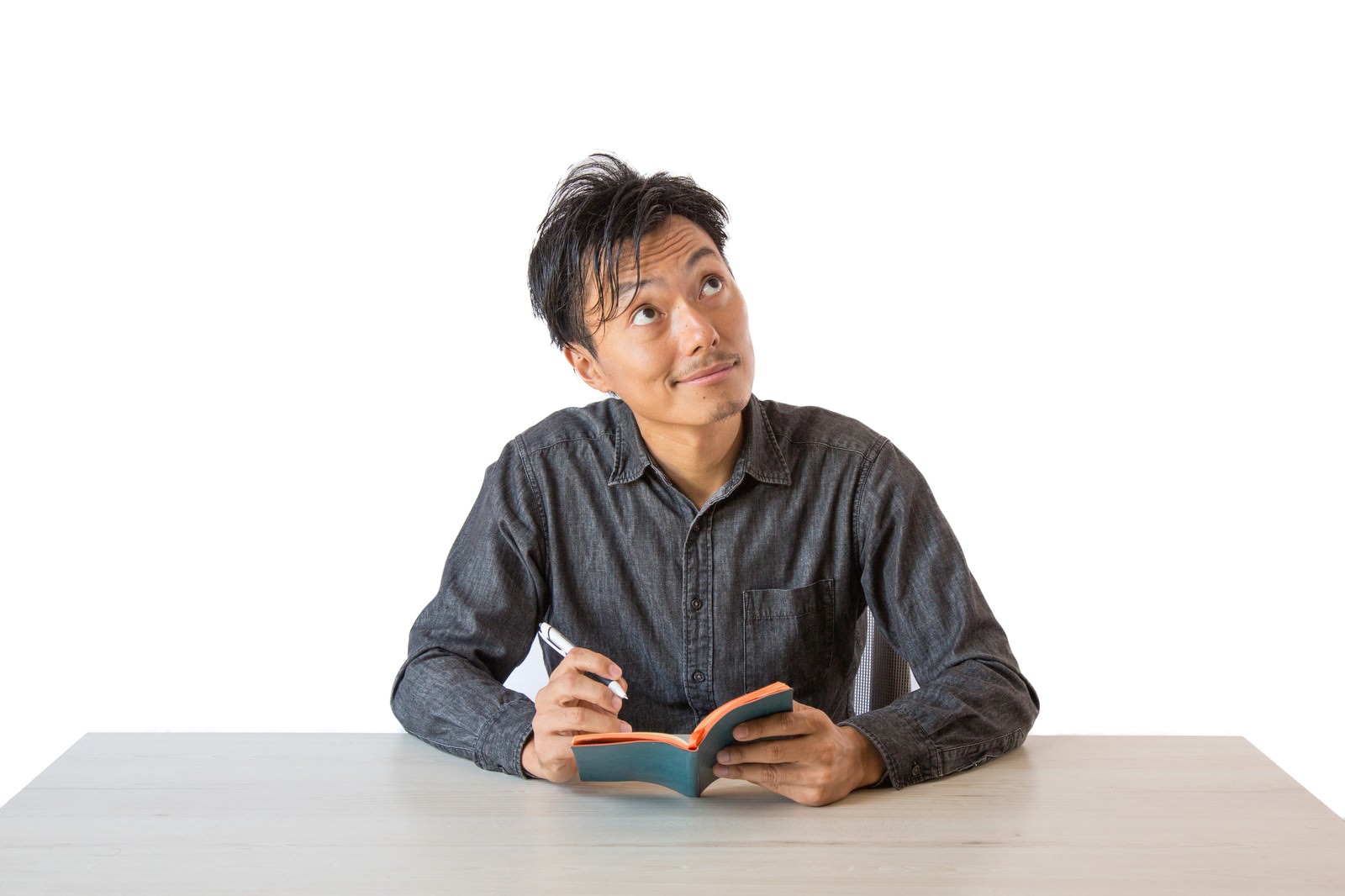 グレーのシャツを着た男性が白い背景で斜め上を見上げながら考え込んでいる［モデル：藤沢篤］
