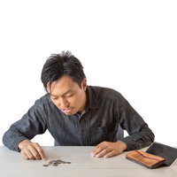 残りの生活費を数えて計算する男性の写真