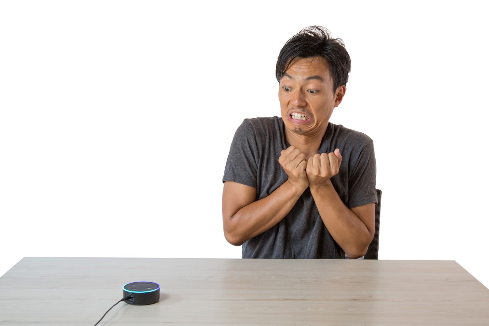 デスクでスマートスピーカーに話しかけて困惑している男性［モデル：藤沢篤］