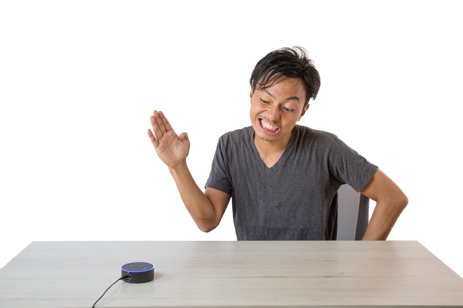 スマートスピーカーに向かって手を挙げて挨拶するグレーシャツの男性［モデル：藤沢篤］
