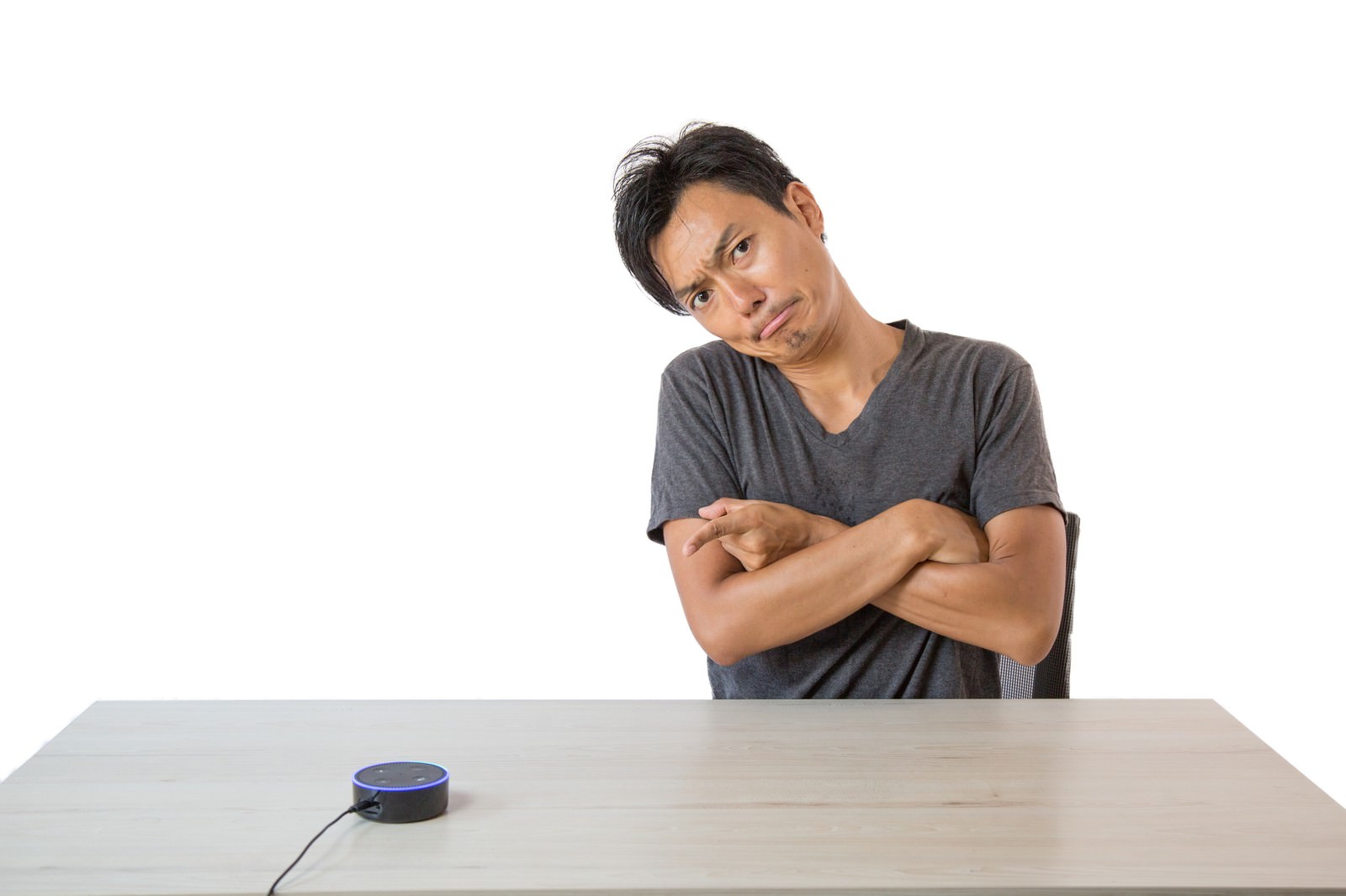 腕組みをして困った表情で首をかしげる男性とテーブル上のスマートスピーカー［モデル：藤沢篤］