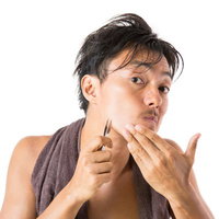 毛抜きで髭の抜き残しを気にして処理する男性の写真