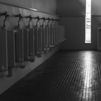 誰もいない男性トイレの一列に並ぶ便器と薄暗い空間の写真