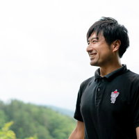 自然に囲まれて爽やかな笑顔を見せる男性インストラクターの写真