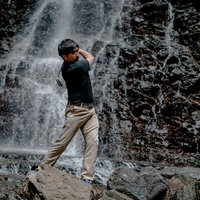 滝の岩場で難しいライからのアプローチショットを打つ男性ゴルファーの写真