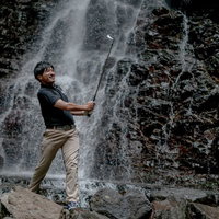 滝と岩場の悪条件下でもゴルフを楽しむゴルファーのインパクトの写真