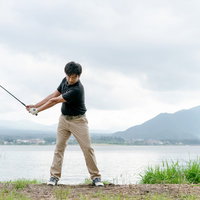 湖と山を背景にするゴルファーのバックスイングの写真