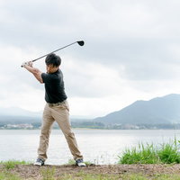 湖畔での理想的なバックスイングを見せるゴルファーの男性の写真