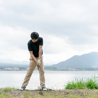 湖と山を背景にしたゴルファーのインパクトの瞬間の写真