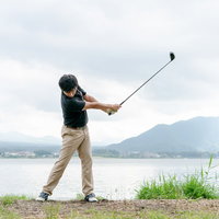 湖畔でゴルフのフォロースイングする男性の動きの写真