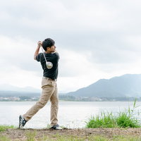 湖と山を背景にドライバーを振るゴルファーの写真