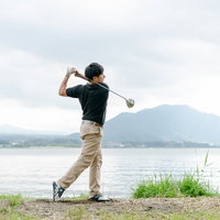 湖と山を背景にしたゴルフスイングのフィニッシュポーズを決める男性の写真