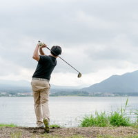 湖畔でゴルフのスイングをするゴルファーのフィニッシュポーズの写真