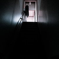 薄暗い古民家の二階から人影が静かに降りてくる階段の写真