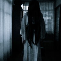 暗い室内でうつむく長髪の女の霊、白い衣服に包まれた怨念の写真
