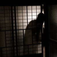 暗い室内の格子窓から覗く女性の人影シルエットの写真