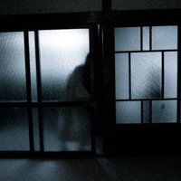 スリガラス越しに見える暗い部屋に入ろうとする人影の写真
