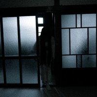 薄暗い古民家の部屋に入る黒髪長髪の女性が立つ怖い風景の写真