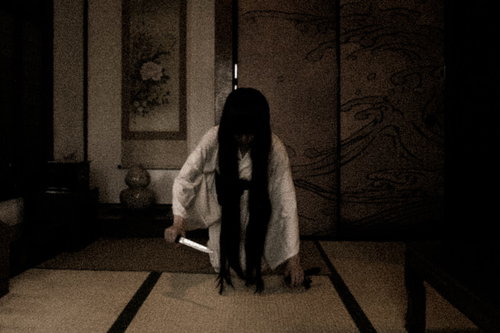 薄暗い和室で刃物を持った白い衣装の幽霊女性が現れた