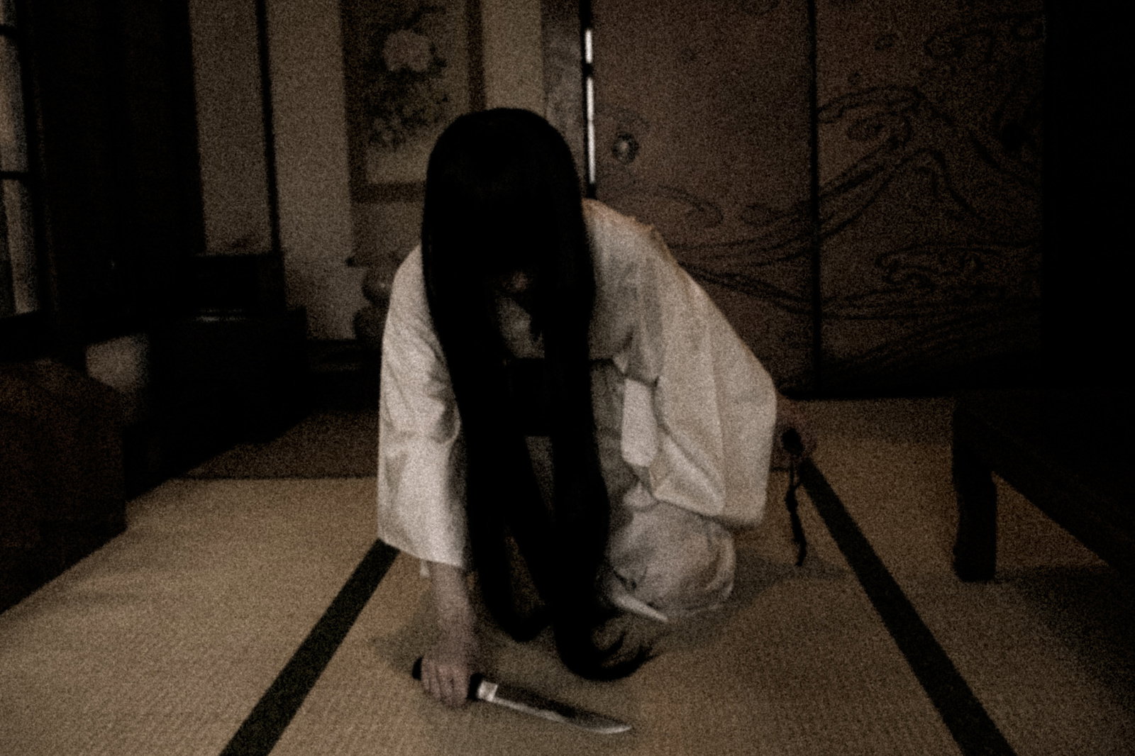 和室で包丁を持つ長髪の幽霊が前かがみに立つ［モデル：緋真煉］