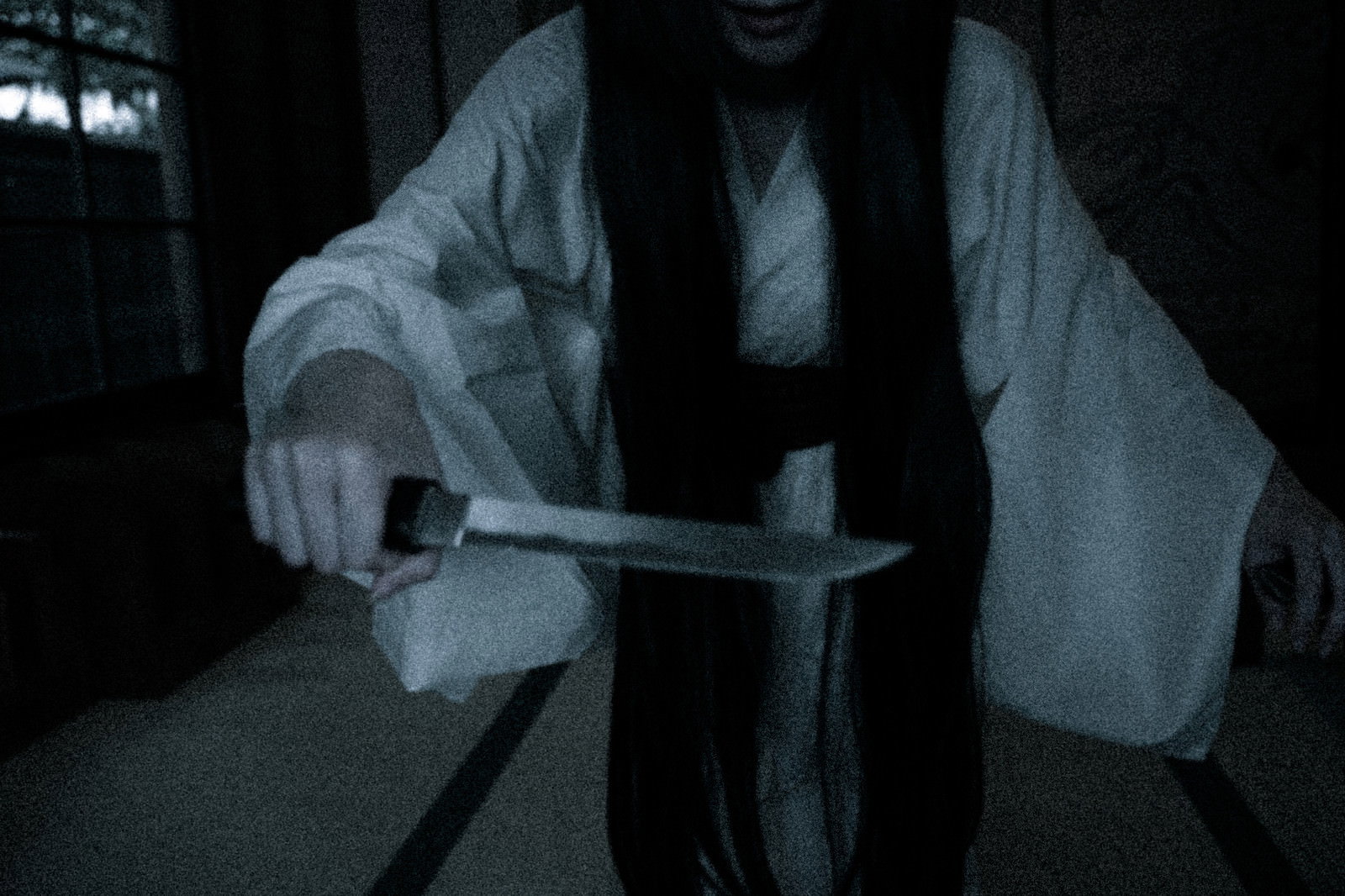 薄暗い場所で短刀を手に持つ白い衣服の女性のホラー写真