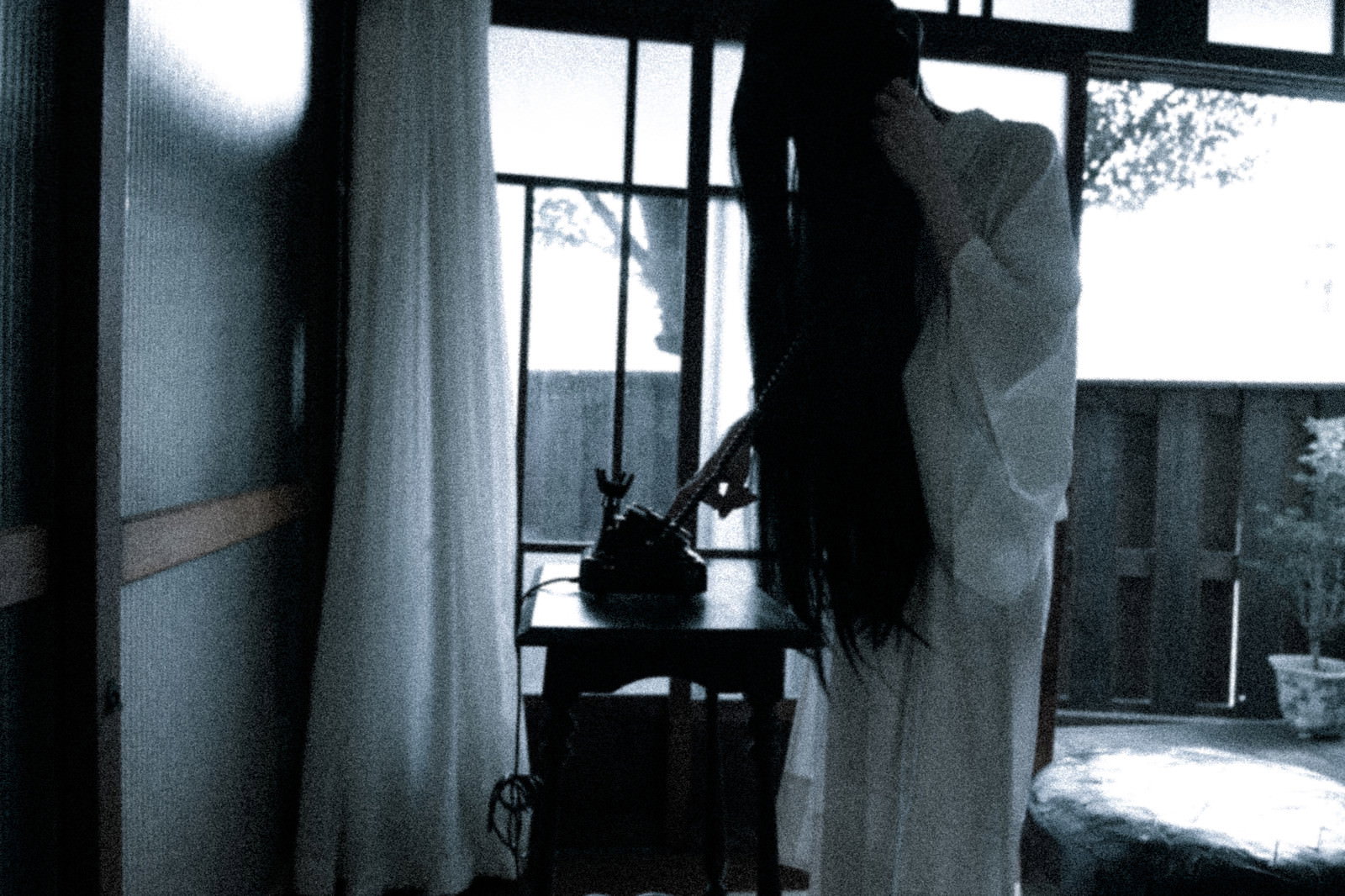 黒電話の受話器を耳に当てて通話している女性［モデル：緋真煉］