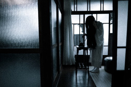 薄暗い室内で呪いの電話をかける女性の後ろ姿