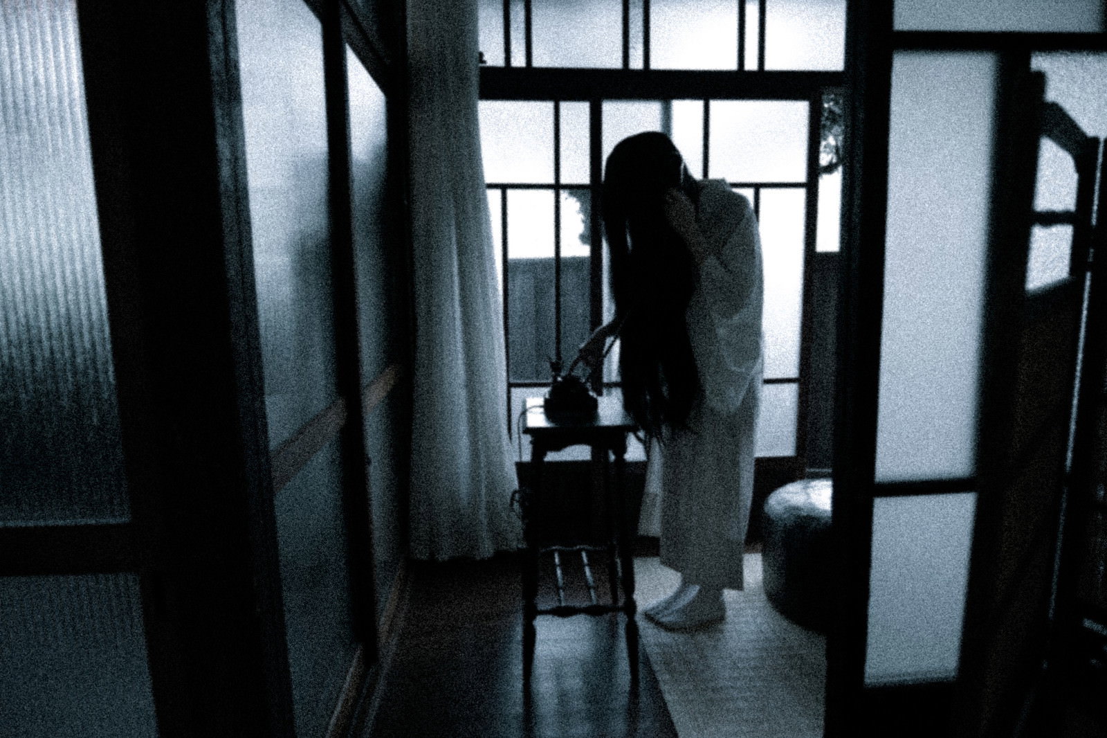 暗い室内で黒電話の前に立つ女性のシルエット、窓からの逆光［モデル：緋真煉］