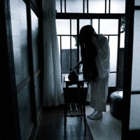 ダイヤル式黒電話から着信する暗い室内で佇む女性のシルエットの写真