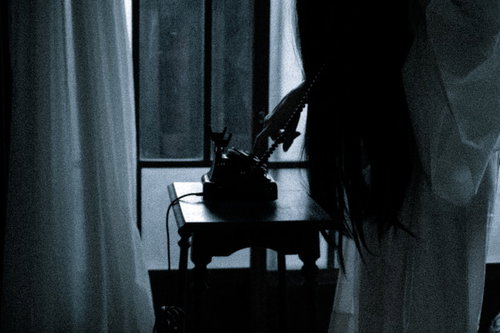 暗い室内で黒電話のダイヤルを回す不気味な女性の姿