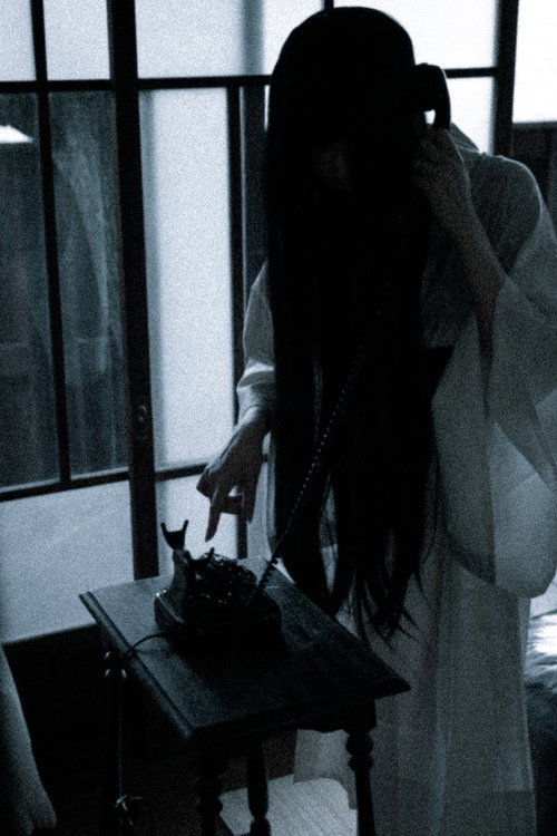 薄暗い部屋で呪いの黒電話を手に取る女性のシルエット