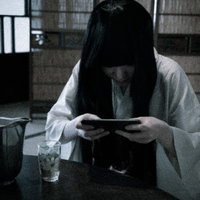 スマホゲームに夢中なサダコさん：暗い部屋で重課金ゲーマーの写真