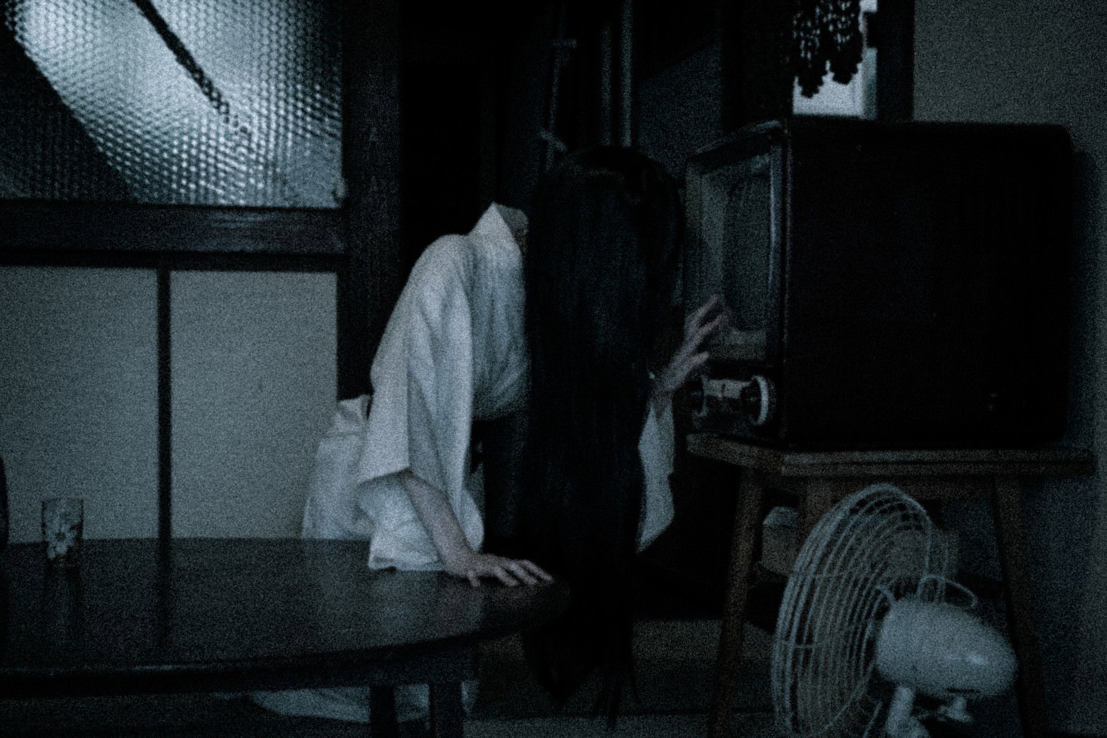 薄暗い部屋のブラウン管テレビから這い出てくる白い髪の人影［モデル：緋真煉］