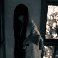 暗い部屋で恨めしそうに手を伸ばす髪の長い幽霊の写真