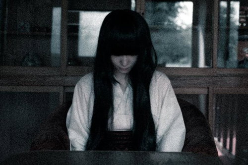 薄暗い室内で俯く長い黒髪の女性の不気味な表情