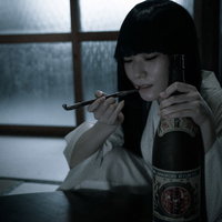 キセルを咥えながら語り始める黒髪の女性と一升瓶の写真