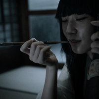 黒いフードを被ってキセルを口に近づける不気味な女性の写真