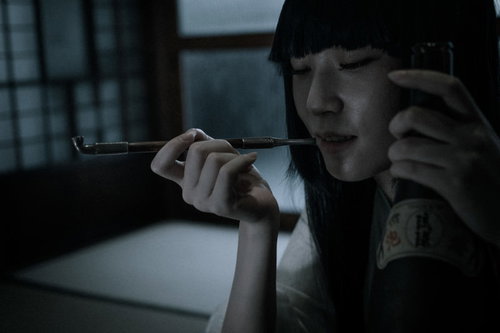 黒いフードを被ってキセルを口に近づける不気味な女性