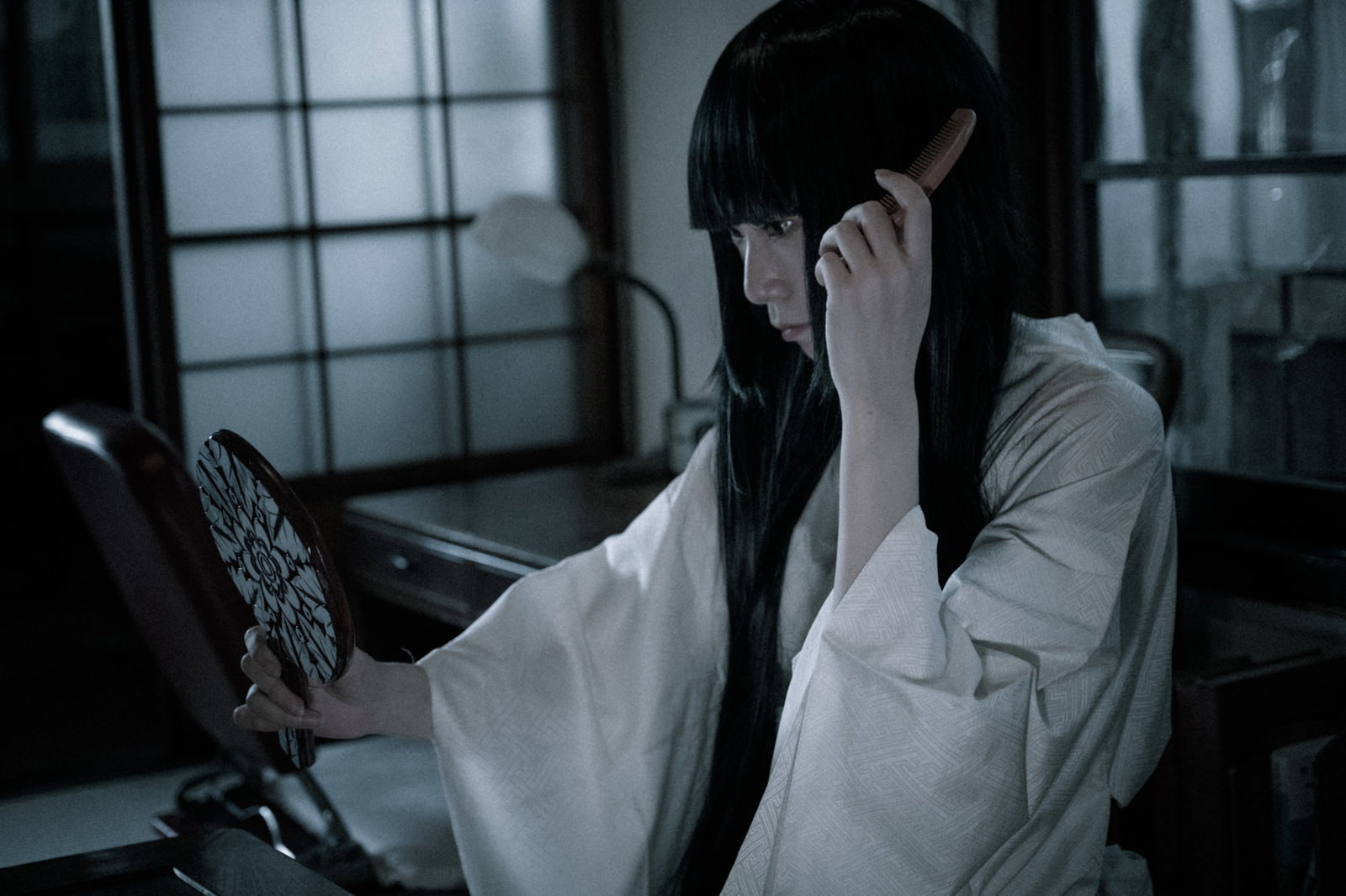 くしで髪をとく長髪の幽霊が白い着物姿で暗い室内に立つ［モデル：緋真煉］