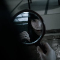 薄暗い室内で円鏡を見ながら髪をとかす女性の写真